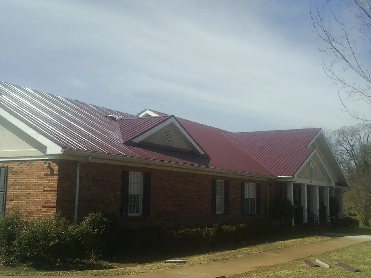 Red metal roof with gabled entries on a long brick building, from a Hail Damage Roof Repair job in Brigham City
