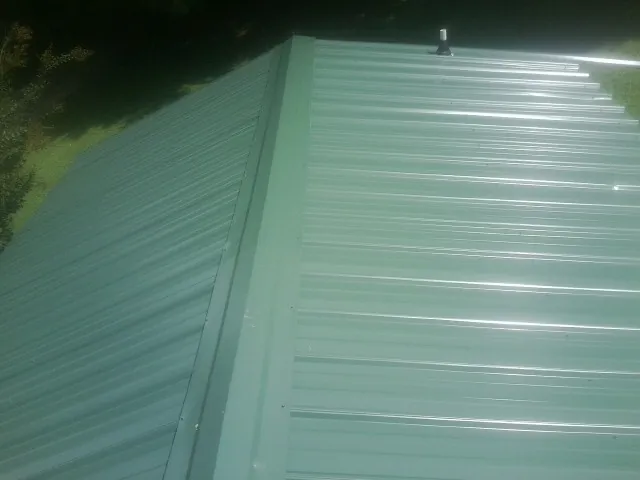 New green metal panels meeting at the ridge of a roof — Flat Roof Repair work by our crew in Brigham City