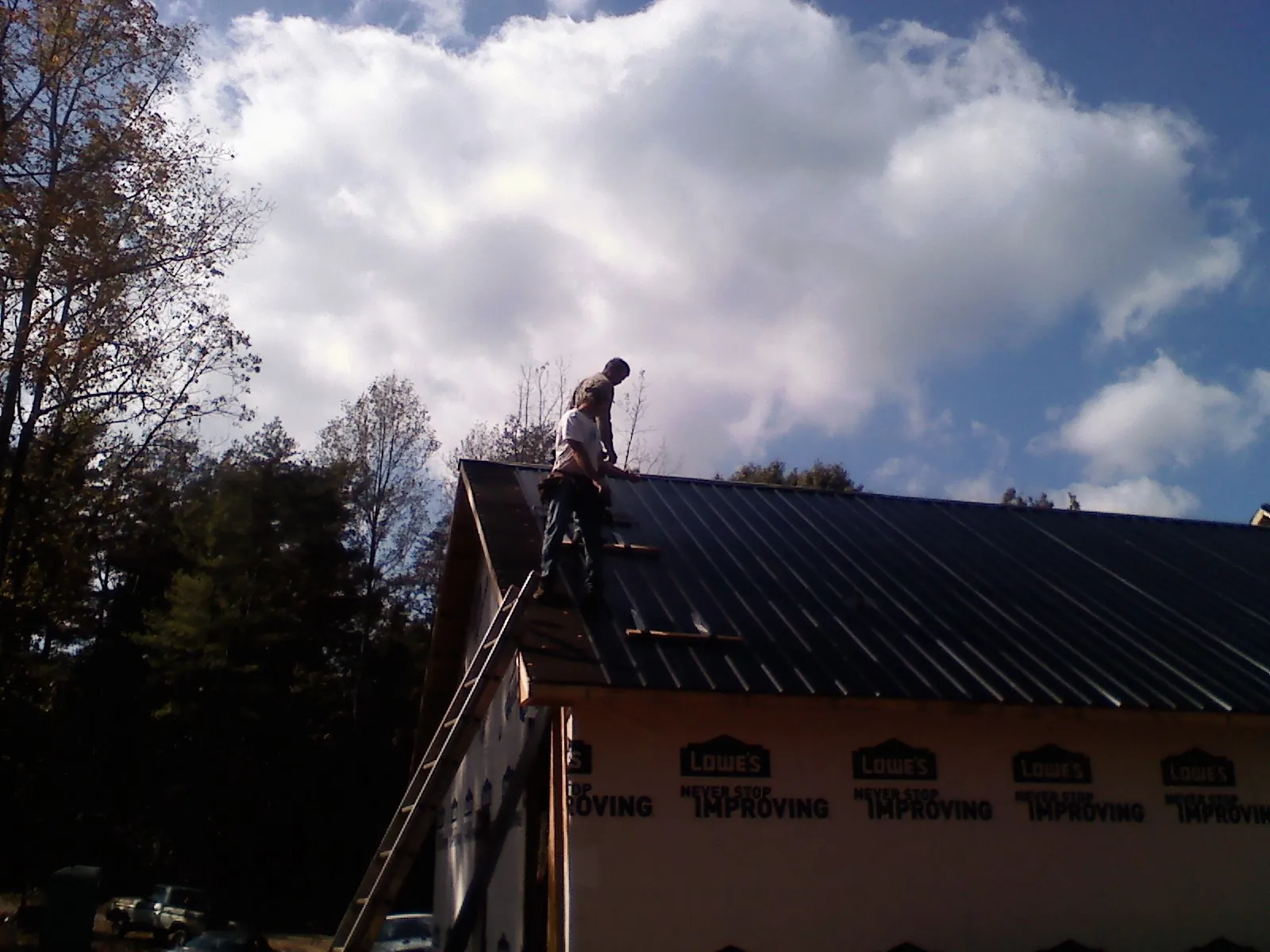 Roofer fastening dark metal panels high against a cloudy sky, from a Roof Inspection job in Brigham City
