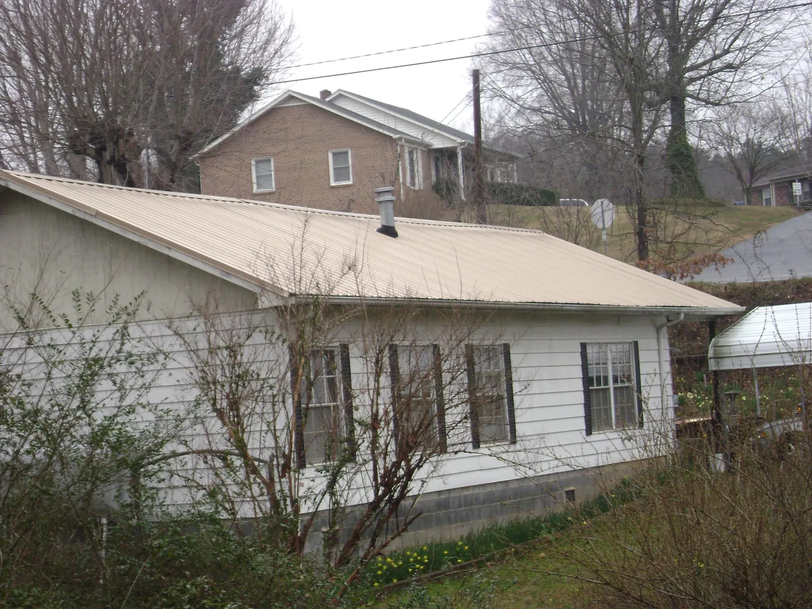 Tan metal roof on a white sided house set into a hillside — Commercial Roofing by Roofing Brothers in Brigham City