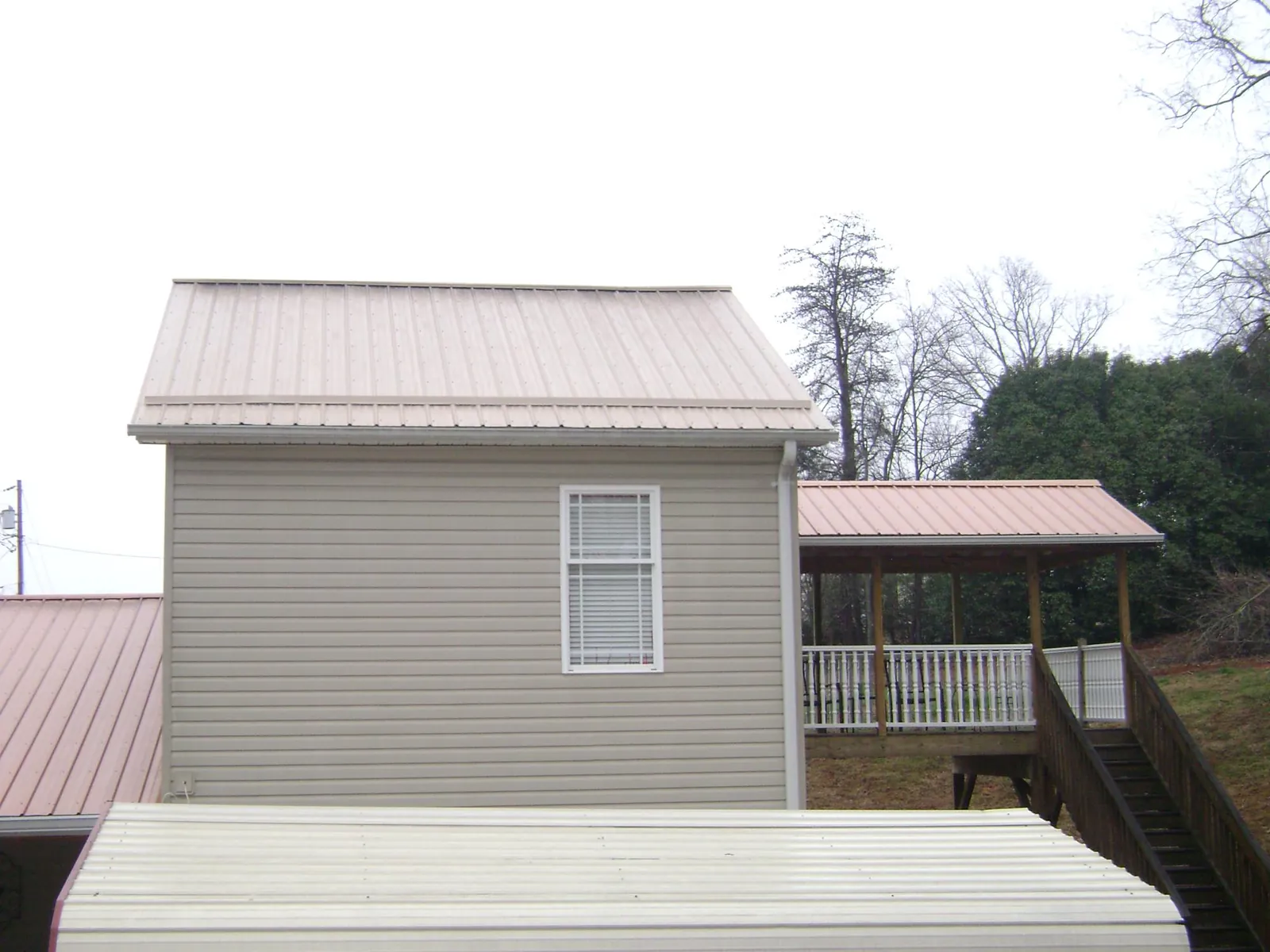Tan metal roofs on a two story addition and attached porch, from a Roof Replacement job in Brigham City
